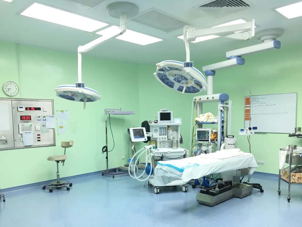 Operation theatre: the operating table under two overhead surgical lights, with the anaesthesia machine and monitors beside it